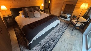 A wooden-paneled bedroom with a large bed, two bedside lamps, a chair, and a mirror.