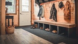 A wooden interior with a bench for shoes, a coat rack, and a door with a window.