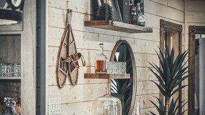 A kitchen with wooden walls, a hanging coat rack, shelves with kitchenware, a table with a lamp, and a potted plant.