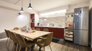 Eine moderne Küche mit einem Holzespeisetisch, Stühlen, einem Edelstahlkühlschrank und einer roten Akzentwand.