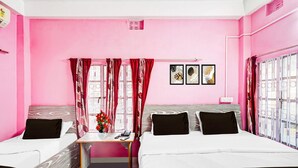 A pink-themed room with two beds, a small table with a vase of flowers, and a window with metal bars. - Hotel O Pradhan Nagar Prince Guest House (Siliguri)