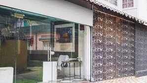 A building entrance with a glass door, a small table with a chair, and a patterned floor. - Hotel O Pradhan Nagar Prince Guest House (Siliguri)
