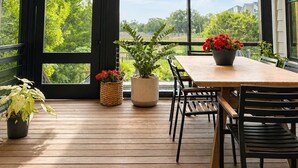 Eine Holzterrasse mit Tisch und Stühlen, großen Fenstern und einem Deckenventilator.