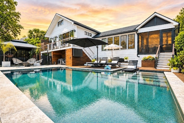 Una casa moderna con piscina, mobiliario exterior y un porche cubierto.