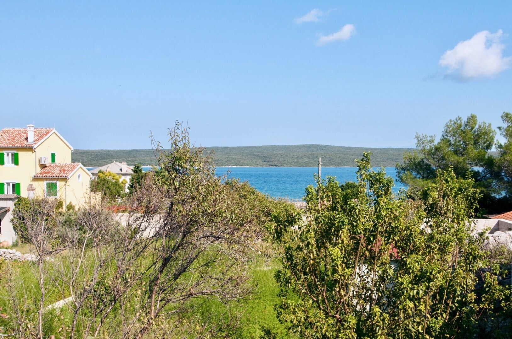 Vista costera con una casa, vegetación y un mar azul cristalino.