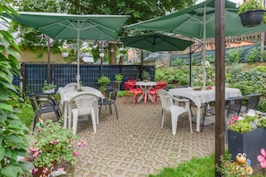 An outdoor patio area with tables and chairs, covered by green umbrellas, surrounded by potted plants and flowers. - Pension Kaufmann / Holiday Apartment for 1–3 Guests in Oberwiesenthal (Oberwiesenthal)