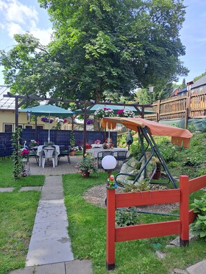 Un jardin avec une balançoire en bois, un sentier et du mobilier d’extérieur.