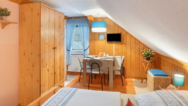 Ein gemütliches Schlafzimmer im Dachgeschoss mit einem Bett, einem kleinen Tisch und einem Stuhl.