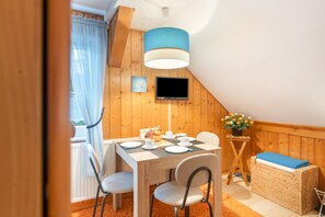 A cozy dining area with a table set for four, a television mounted on the wall, and a wicker basket with flowers.