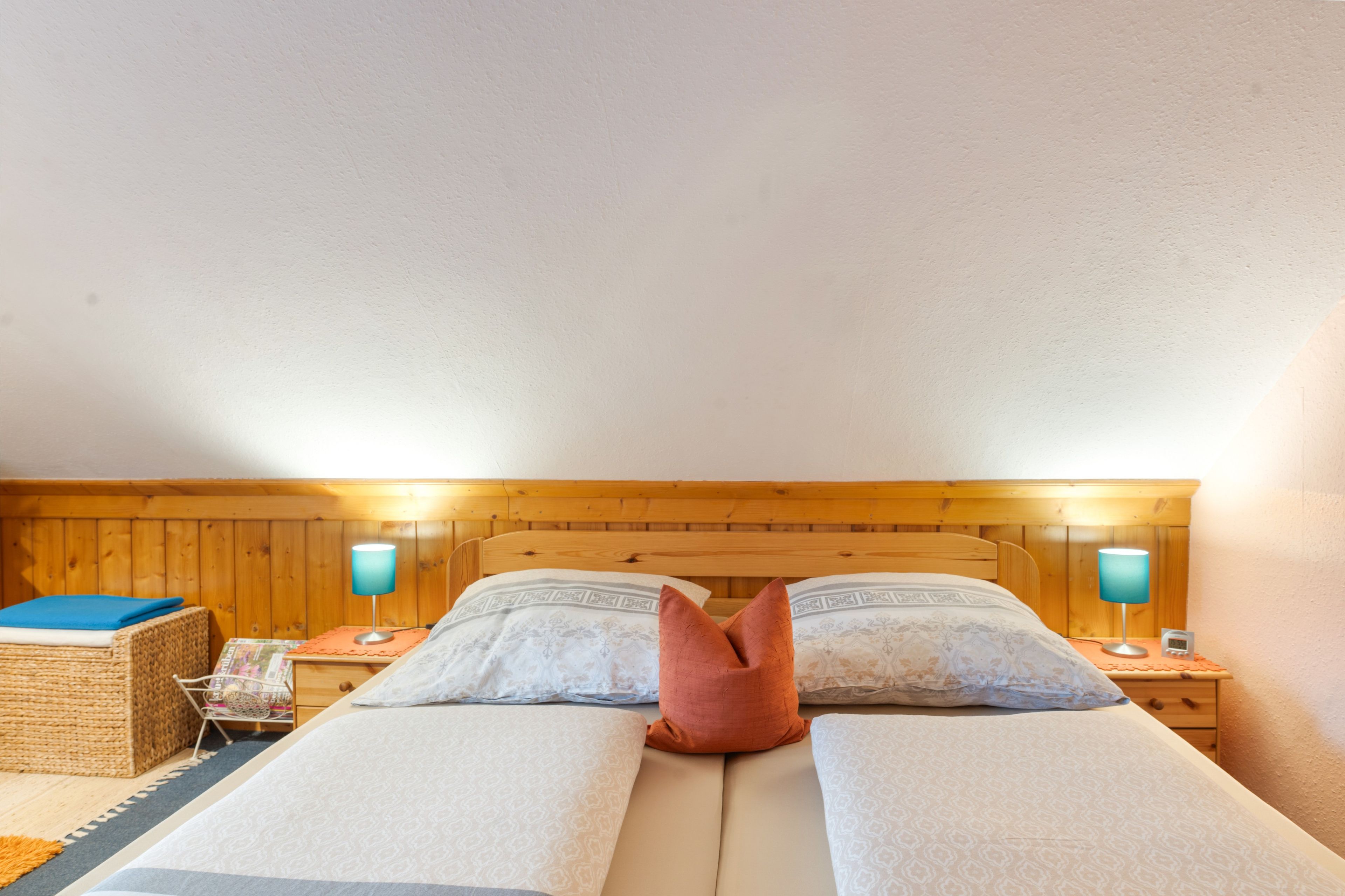 Ein Doppelbett mit Holz-Kopfteil, zwei Nachttische mit Lampen und ein kleiner Tisch ebenfalls mit einer Lampe.