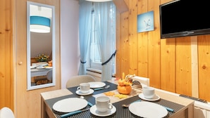 Ein Hotelzimmer mit Esstisch für zwei Personen, einem an der Wand montierten Fernseher und einem Fenster mit Vorhängen.