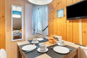 A hotel room with a dining table set for two, a television mounted on the wall, and a window with curtains. - Pension Kaufmann / Holiday Apartment for 1–3 Guests in Oberwiesenthal (Oberwiesenthal)