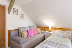 A bedroom with a grey sofa, a wooden headboard, a bedside table with a lamp, and a bed with patterned bedding.