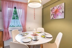 Un coin repas avec une table ronde dressée pour quatre personnes, des chaises blanches et une décoration florale fixée au mur.