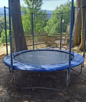 A trampoline surrounded by a wooden fence, with trees and a distant view of mountains. - Pension Kaufmann / Holiday Apartment for 2 to 4 Guests in Oberwiesenthal (Oberwiesenthal)