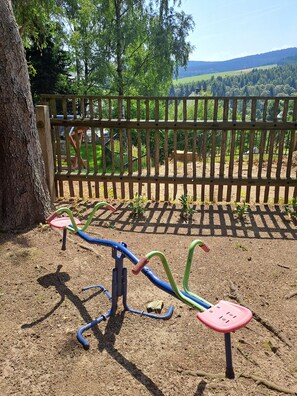 An outdoor exercise equipment area with a wooden fence and trees in the background.
