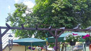En udendørs patio med borde og stole, omgivet af krukker med planter og en pergola med blomsterkurve.