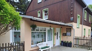 En toetagers bygning med en træfacade, en hvid bænk foran og et skilt der angiver en virksomhed eller et etablissement.
