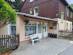 Un bâtiment à deux étages avec une façade en bois, un banc blanc à l’extérieur et une enseigne indiquant un commerce ou un établissement.