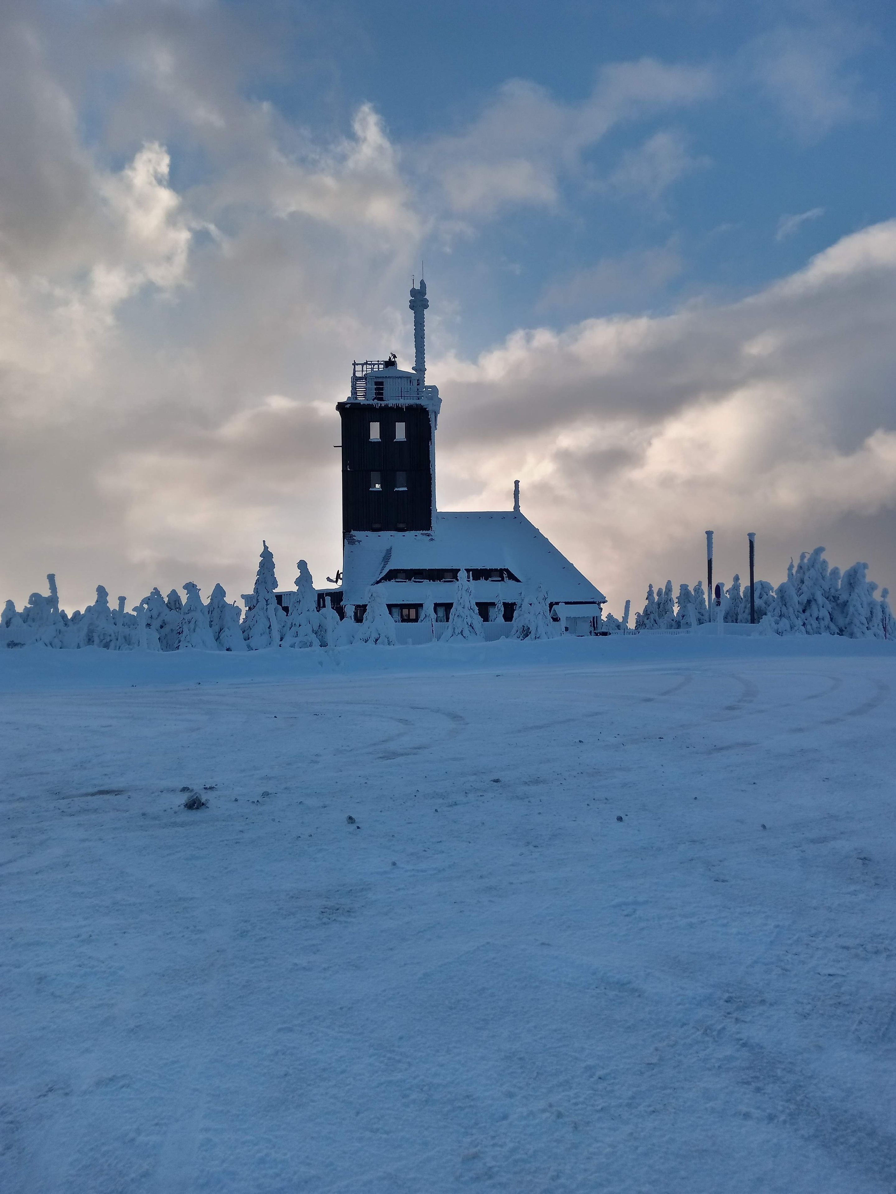 A snow-covered building with a prominent tower, surrounded by snow-laden trees.