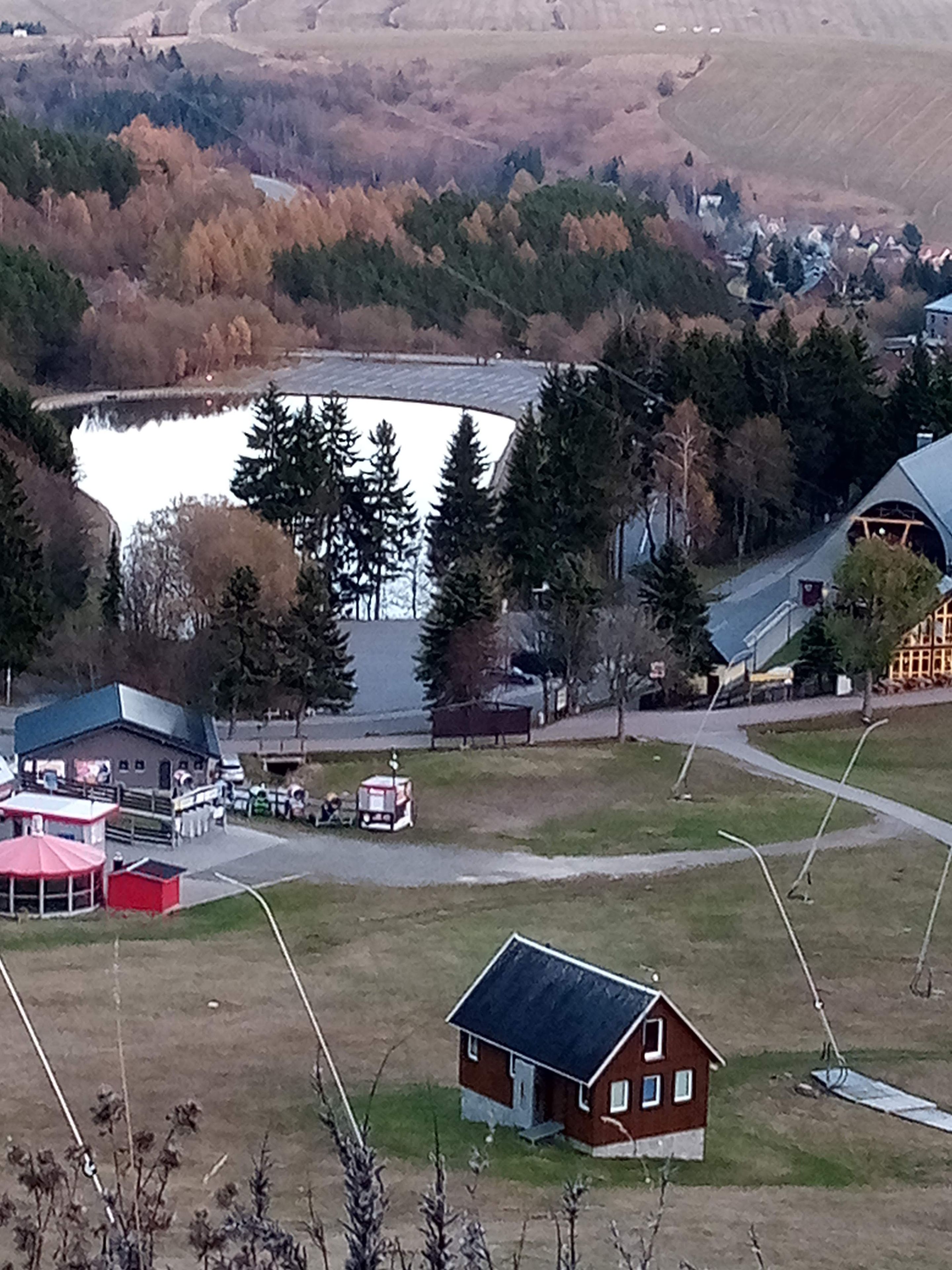 A rural landscape with a lake, a small house, and a building with a sloped roof.
