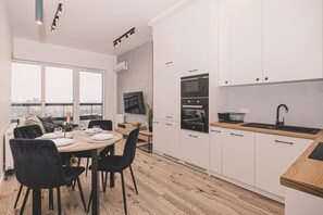 Une cuisine moderne avec des meubles blancs, un plan de travail en bois et un coin repas avec une table dressée pour quatre personnes.