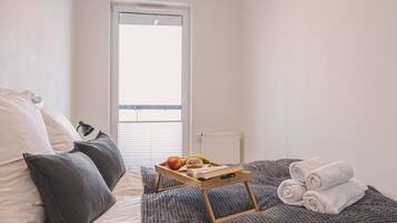Een slaapkamer met een bed, kussens, een dienblad met fruit en een boek, een raam en een radiator.