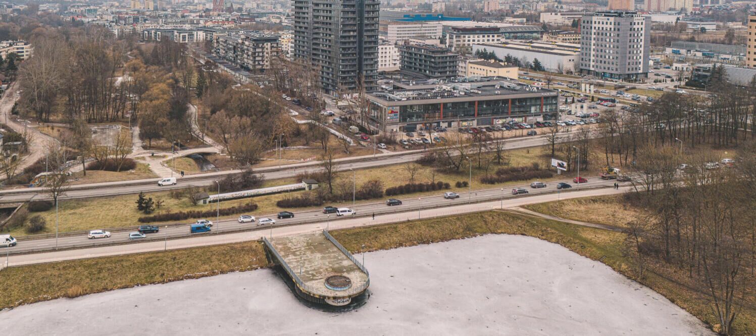 Vista aérea de um horizonte urbano com uma autoestrada, edifícios e um parque de estacionamento amplo e vazio.