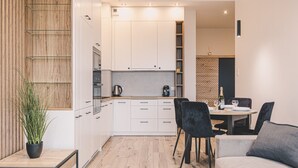 Une cuisine moderne avec des meubles blancs, un coin repas comprenant une table et des chaises, et une plante en pot.