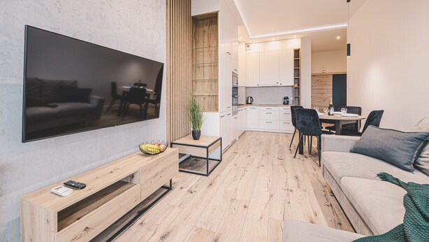 Un salon moderne doté d’un téléviseur à écran plat, de parquet, d’un canapé, d’une table basse et d’un coin repas avec des chaises et une table.