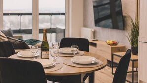 Un coin repas avec une table ronde dressée pour quatre personnes, une bouteille de champagne et un téléviseur fixé au mur.