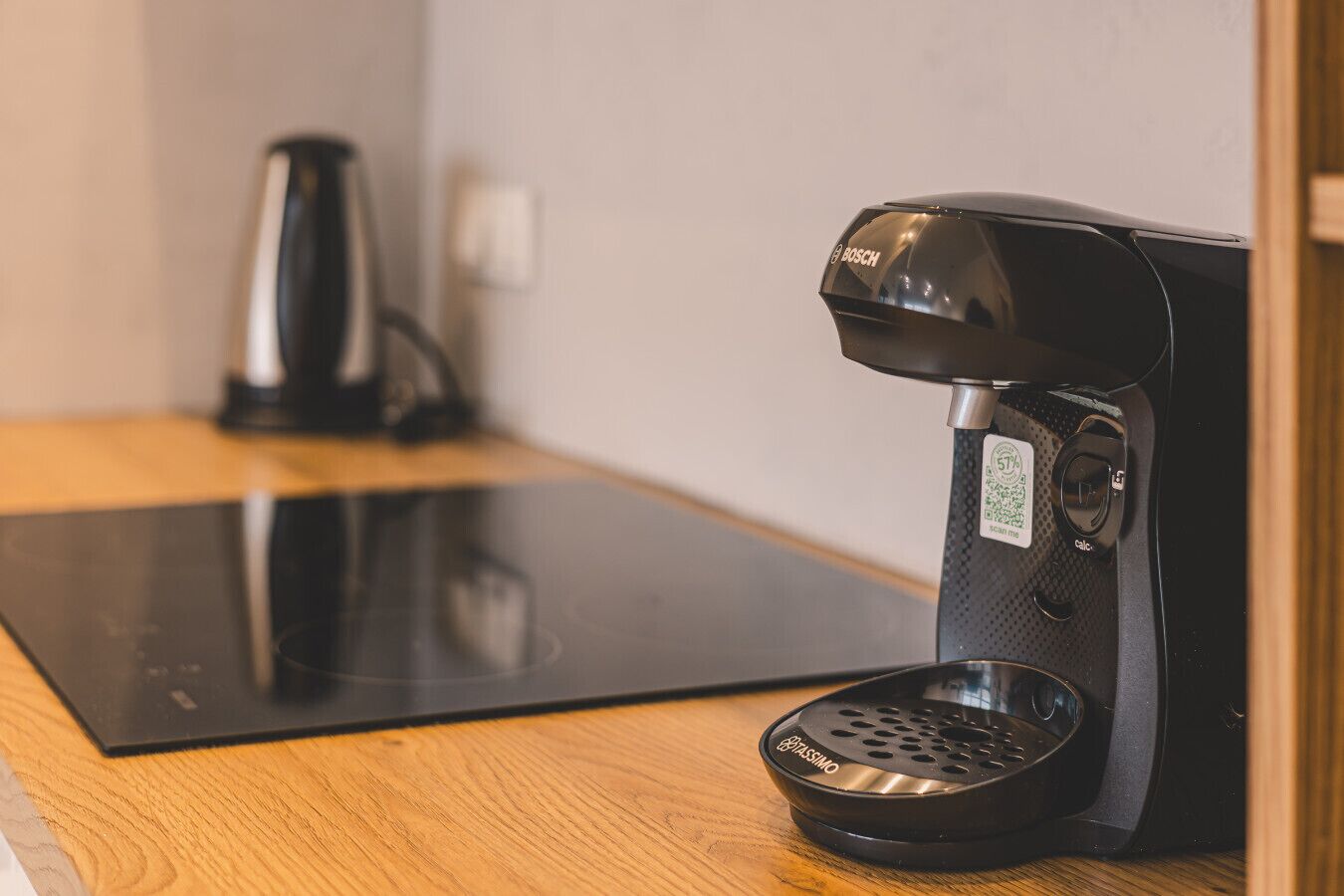 A black coffee maker on a wooden countertop with a black induction cooktop in the background.