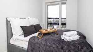Une chambre moderne avec un lit, des oreillers, un plateau de pâtisseries et une vue dégagée sur l’extérieur grâce à une grande fenêtre.