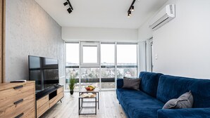 Un salon moderne doté d’un grand téléviseur, d’un canapé bleu, d’un meuble en bois et d’une grande fenêtre offrant une vue sur la ville.