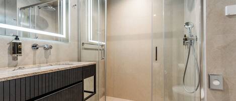 A modern bathroom with a glass-enclosed shower, a large mirror, and a dark wood vanity.