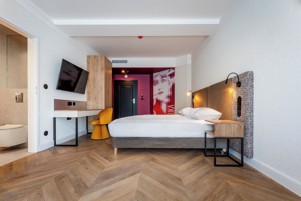 Een moderne hotelkamer met een bed, bureau, stoel, televisie en badkamer.