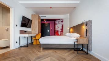Moderni hotellihuone, jossa on sänky, työpöytä, tuoli, televisio ja kylpyhuone.