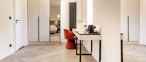 Een moderne hotelkamer met een visgraatvloer, een bureau met lamp, een stoel en een bed op de achtergrond.