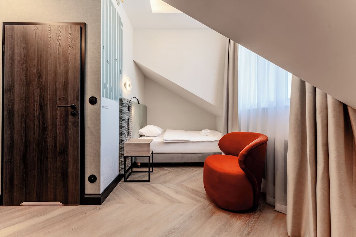 Een moderne hotelkamer met een houten deur, een bed met witte lakens, een rode stoel en een dakraam.