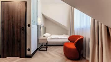 Et moderne hotelværelse med dør i træ, seng med hvide sengetøj, en rød lænestol og et ovenlys.