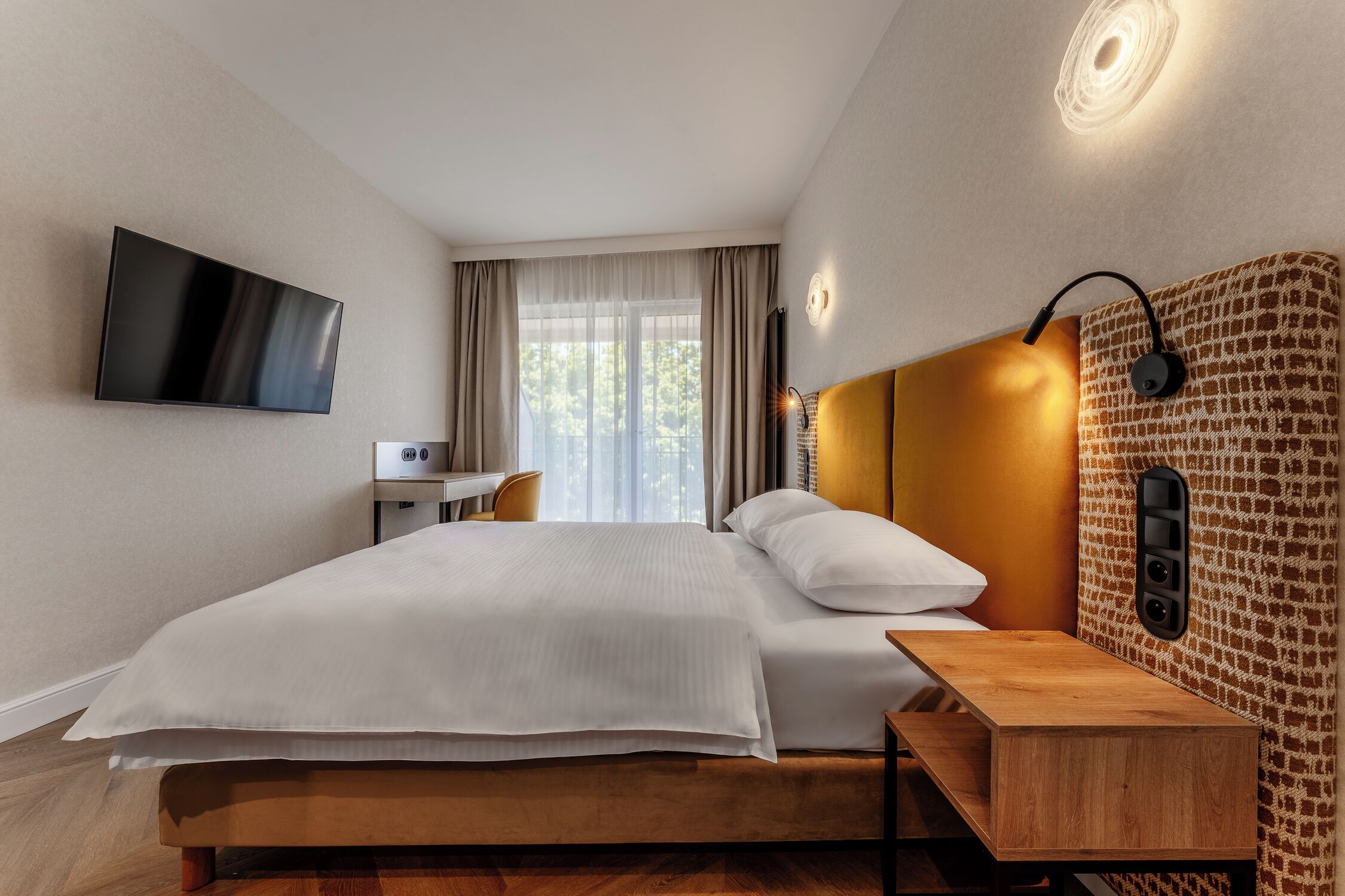 Ein Hotelzimmer mit Bett, Nachttisch, Fernseher und einer Wandleuchte.