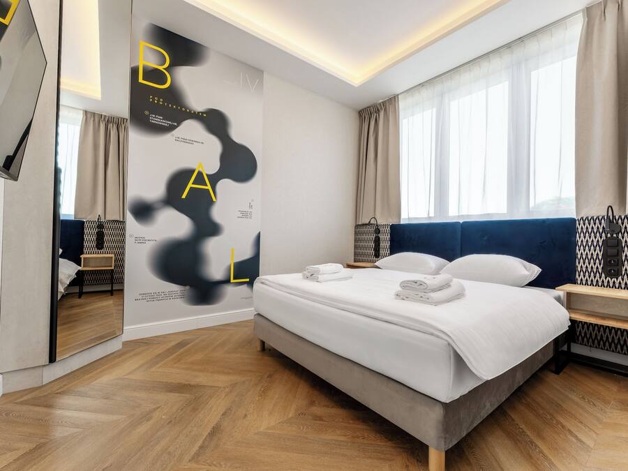 A modern hotel room with a large bed, a TV, and a view of the city.
