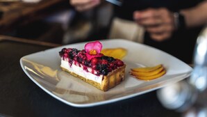 A dessert on a white plate with a pink flower garnish, accompanied by fruit slices on the side. - Villa Sara Resort (Venezia)