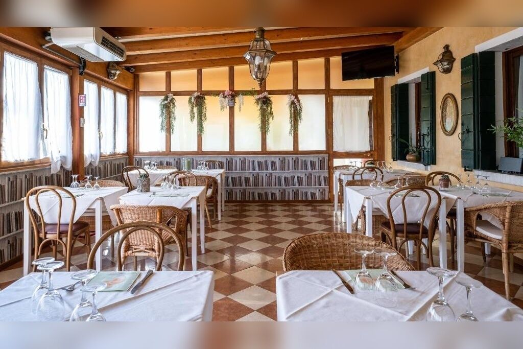 Un restaurant au sol à carreaux, avec des nappes blanches, des chaises en osier et des plantes suspendues.