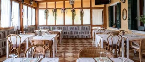 Un restaurant au sol à carreaux, avec des nappes blanches, des chaises en osier et des plantes suspendues.