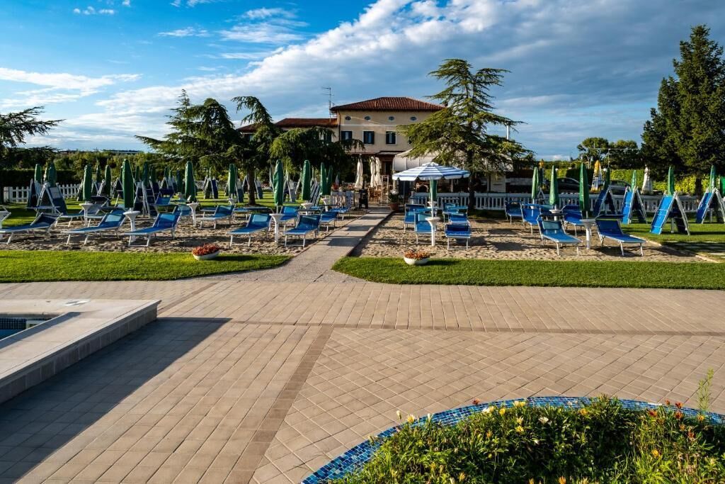 A poolside area with lounge chairs and umbrellas, a building with a red roof, and a clear sky.