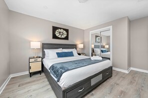 Une chambre à coucher comprenant un lit, des tables de chevet, un miroir et une œuvre d’art murale.