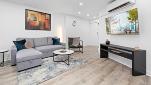 Una sala de estar moderna con un sofá seccional gris, una mesa de centro redonda, un aparador negro y un televisor de pantalla plana grande montado en la pared.