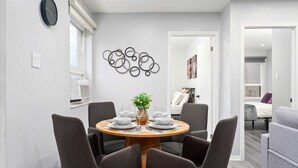 A dining area with a round table, six chairs, a clock, and a wall art piece. - Modern Suite Near Dufferin Grove Transit Line (Toronto)