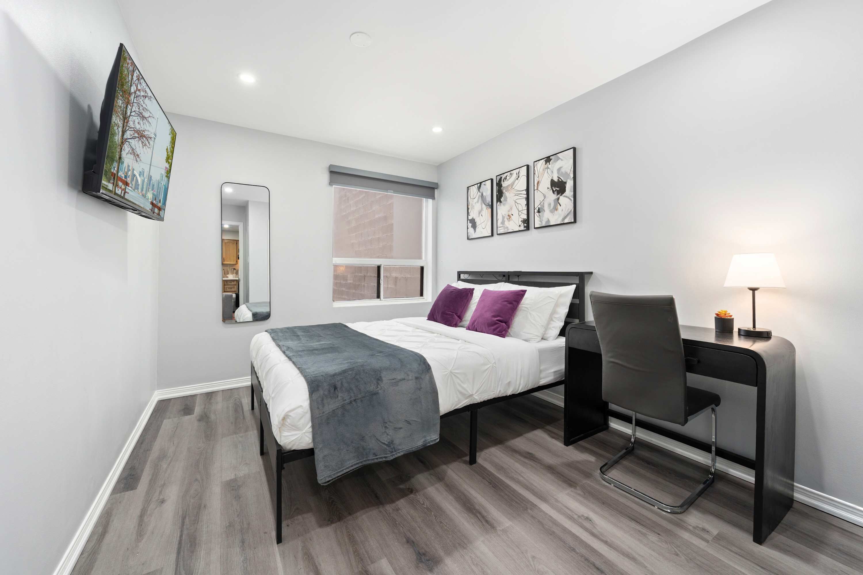 A modern bedroom with a bed, desk, chair, and artwork on the wall.